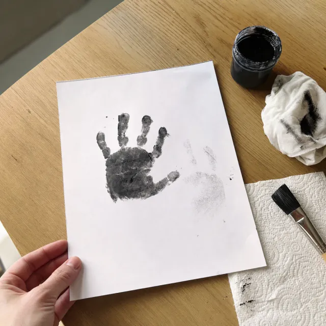 Messy baby handprint in blue poster paint on white paper with smudges on the table